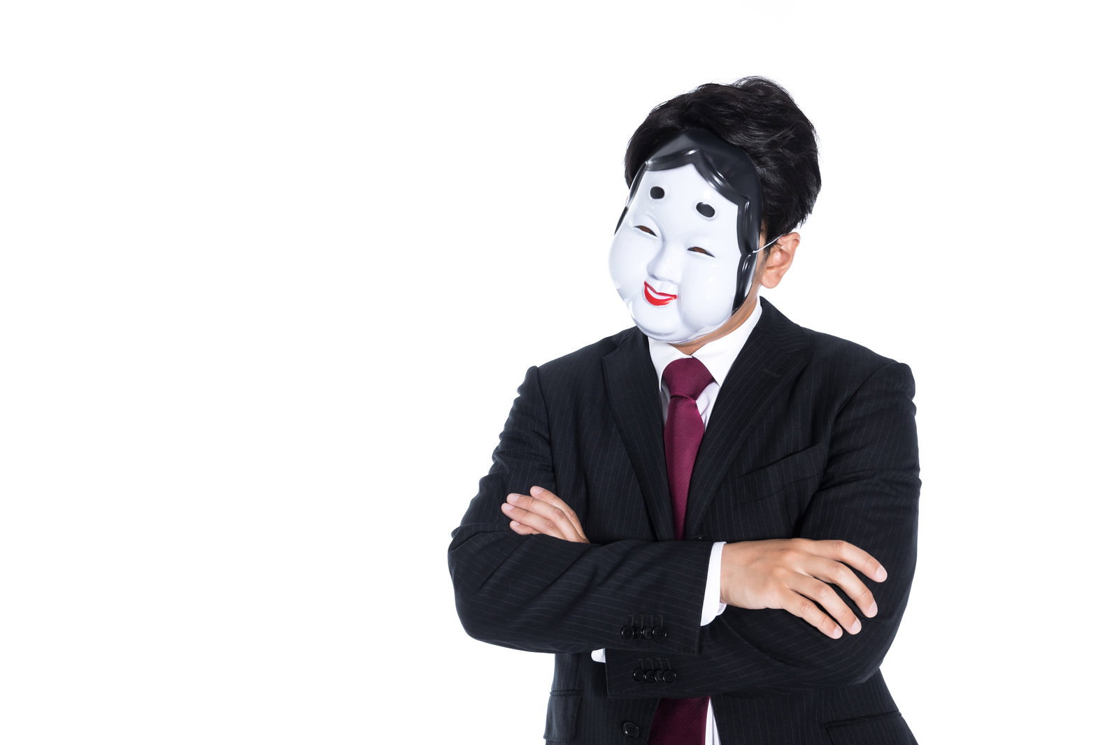 白いおかめのお面を着けて黒いスーツで腕を組む男性［モデル：大川竜弥］