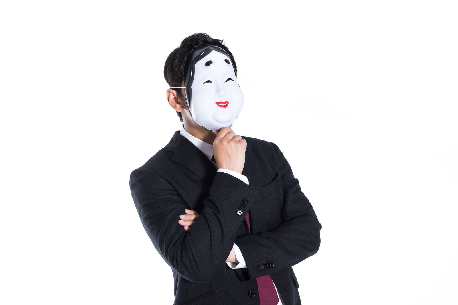 白いお面を被って黒いスーツを着た男性が考える仕草をしている［モデル：大川竜弥］