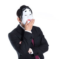 騙された人間を見て笑うおかめをかぶった黒スーツの男性の写真