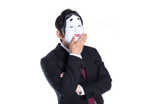 騙された人間を見て笑うおかめをかぶった黒スーツの男性