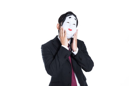 表面上はニコニコしているおかめのお面をつけたスーツ姿の男性