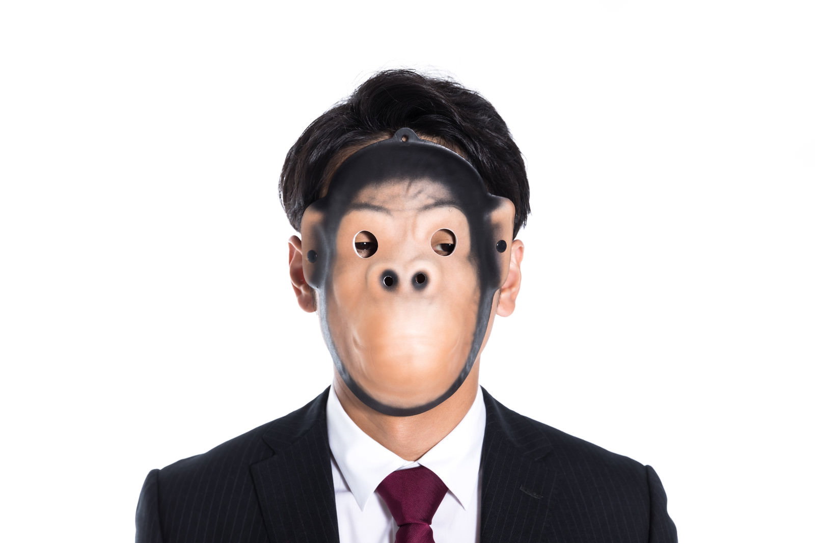 黒いスーツと赤いネクタイを着た男性が猿のお面をつけている［モデル：大川竜弥］