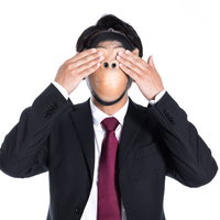 両手で目を覆う見ざるのスーツ姿の男性、暗闇の中で見ないという仕草の写真