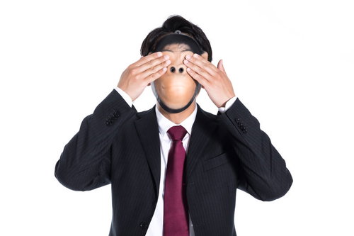 両手で目を覆う見ざるのスーツ姿の男性、暗闇の中で見ないという仕草