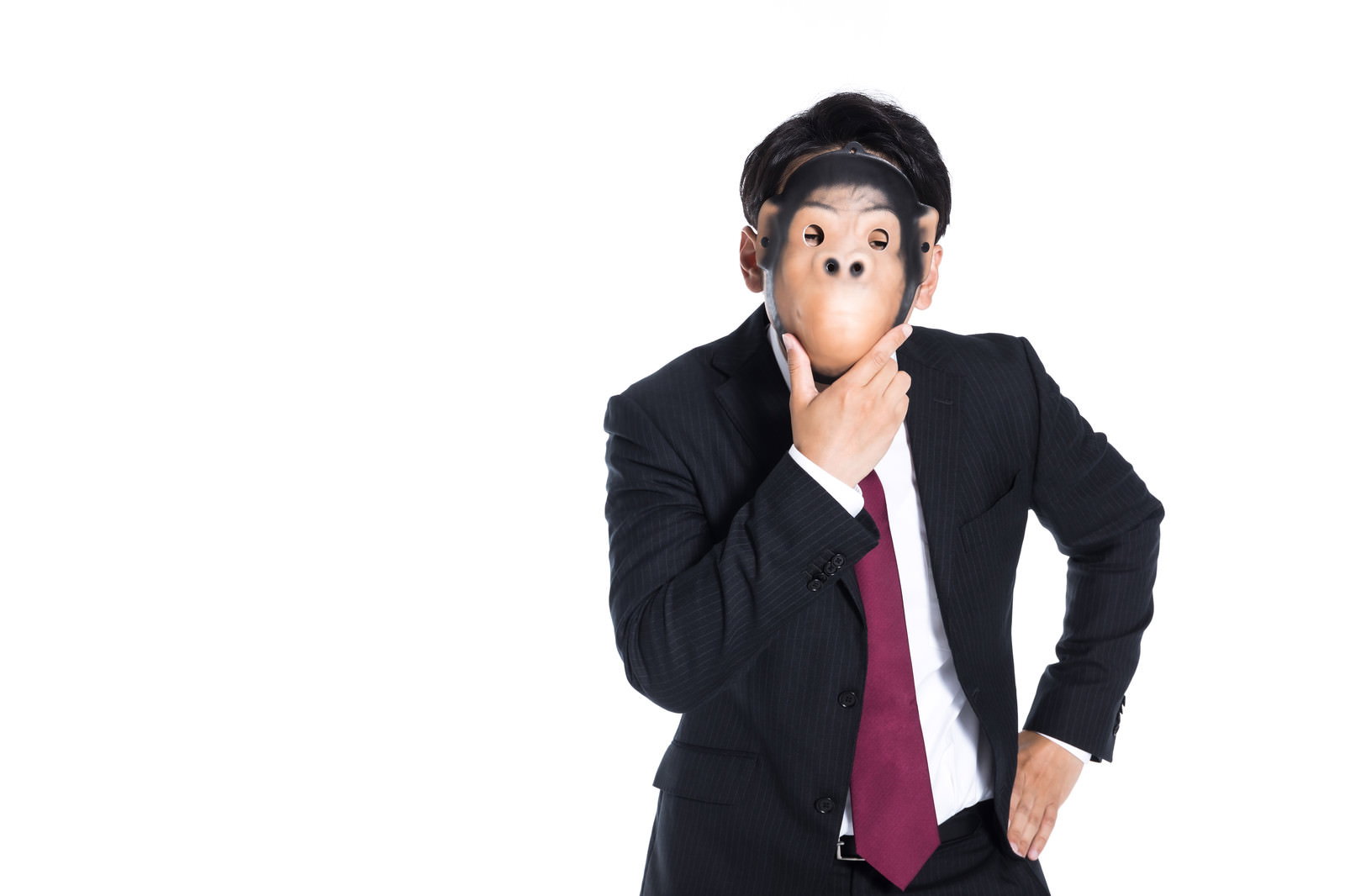 お面をつけて考えるポーズをとるスーツ姿の会社員［モデル：大川竜弥］