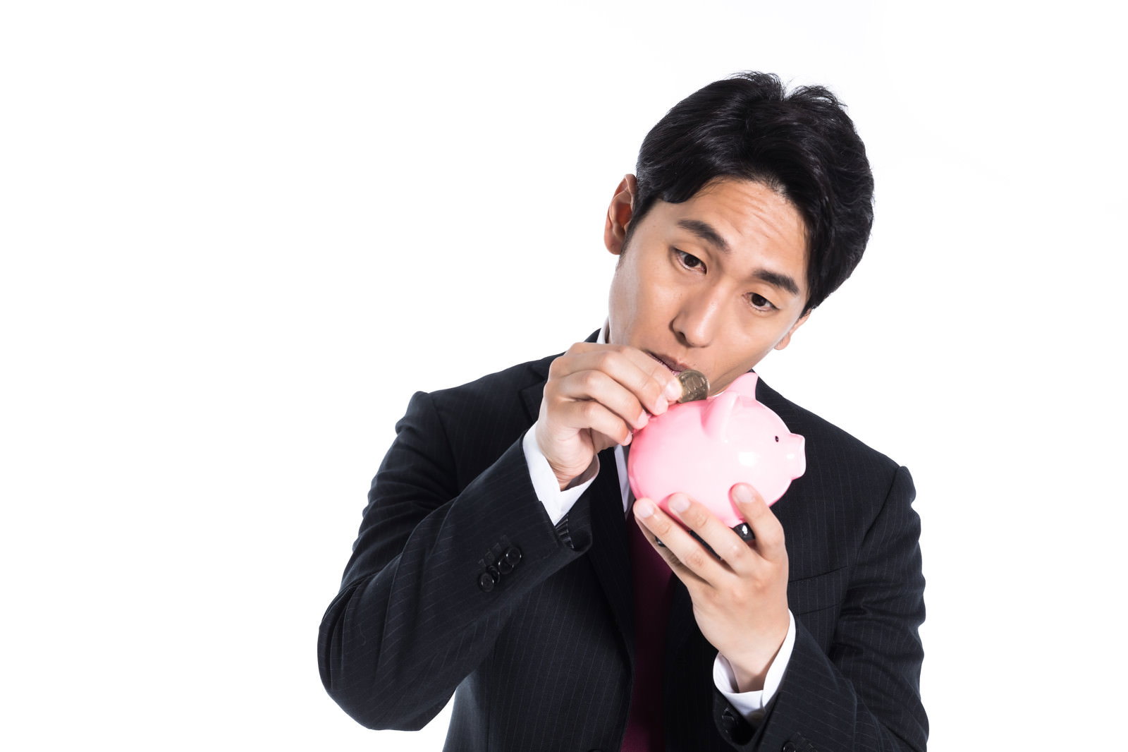 ピンク色の貯金箱に小銭を入れるスーツ姿のサラリーマン男性［モデル：大川竜弥］