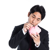ピンク色の貯金箱に小銭を入れるサラリーマンの写真