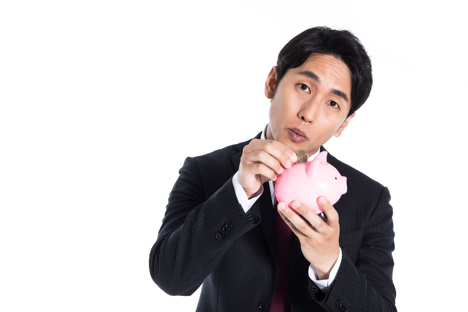 ピンクの貯金箱を抱えて微笑むスーツ姿の男性［モデル：大川竜弥］