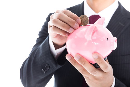 500円玉をピンク色のブタの貯金箱に入れるスーツ姿の男性