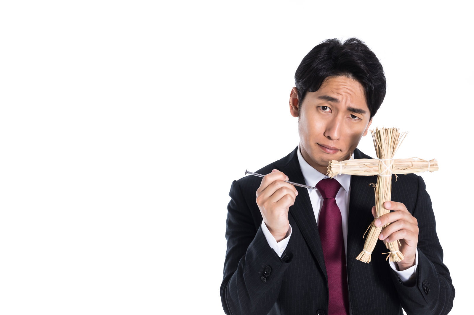 藁人形と五寸釘を持ち不気味な表情を浮かべるスーツ姿の営業マン［モデル：大川竜弥］