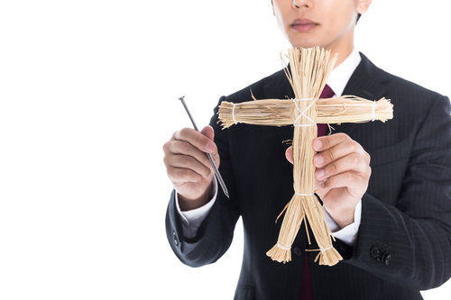 藁人形、今なら五寸釘もセットです。黒いスーツの男性が手に持つ