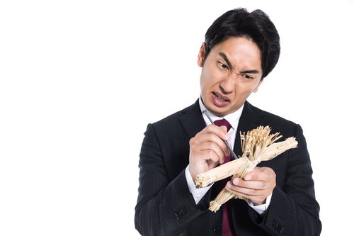 黒いスーツのサラリーマンが藁人形に五寸釘を刺す
