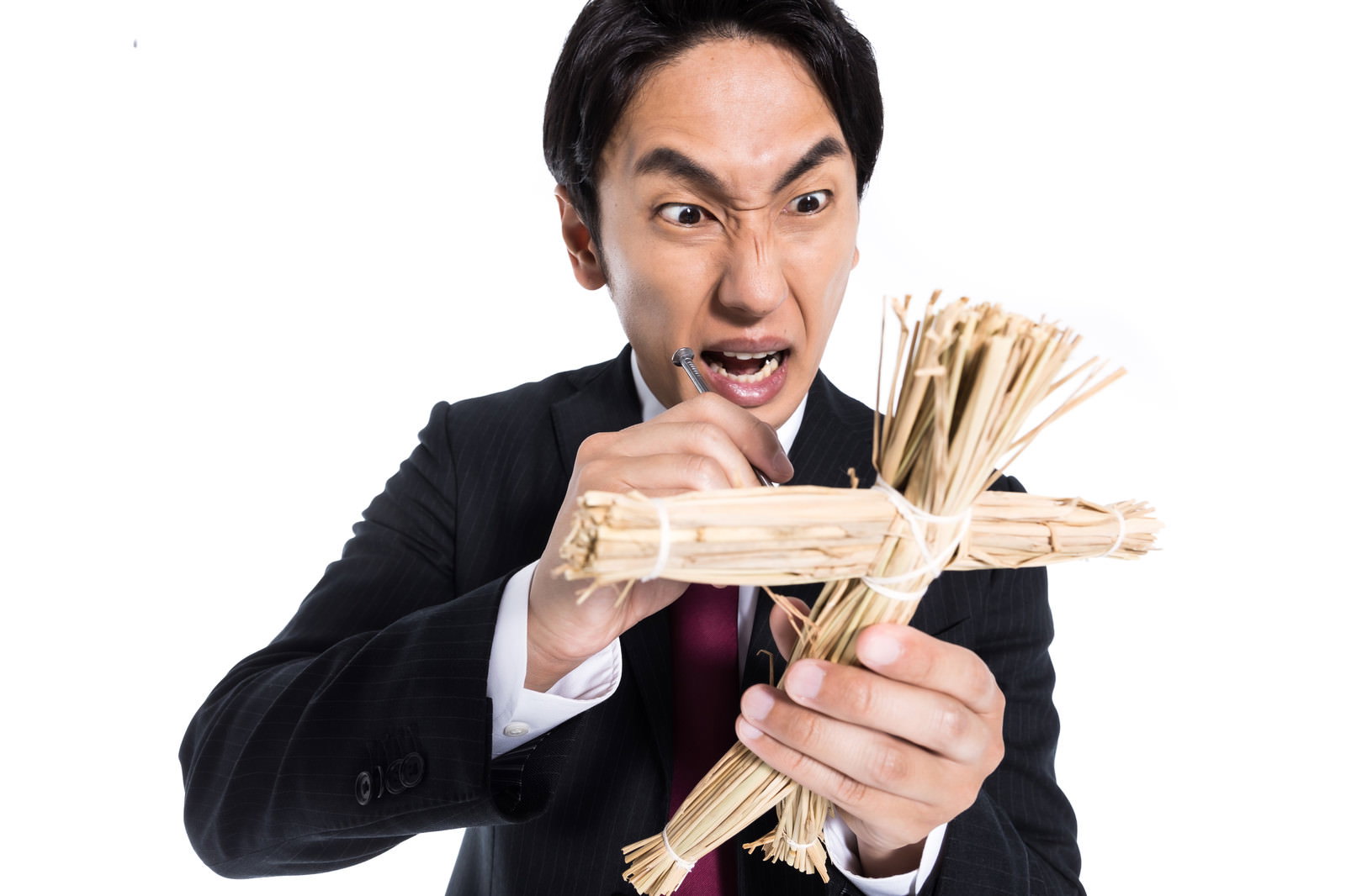 藁人形と五寸釘を持ち激しい表情で怒りを表現する黒いスーツの会社員男性［モデル：大川竜弥］