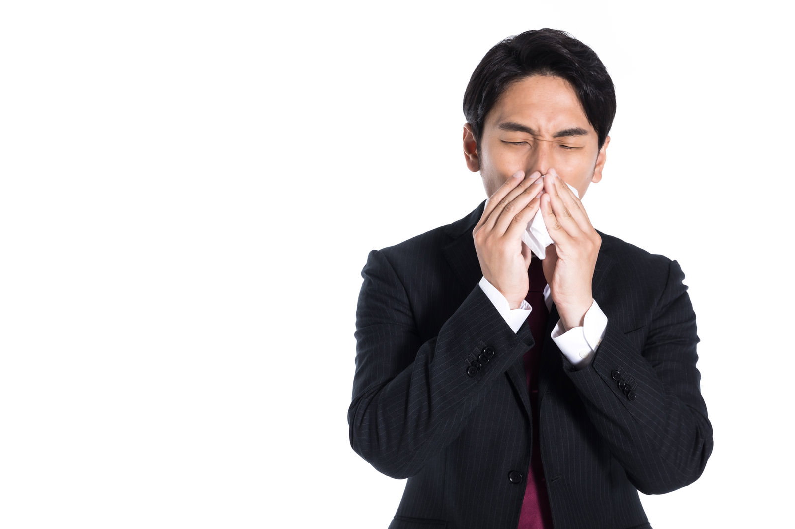 白いティッシュで鼻をかんでいるスーツ姿の男性［モデル：大川竜弥］