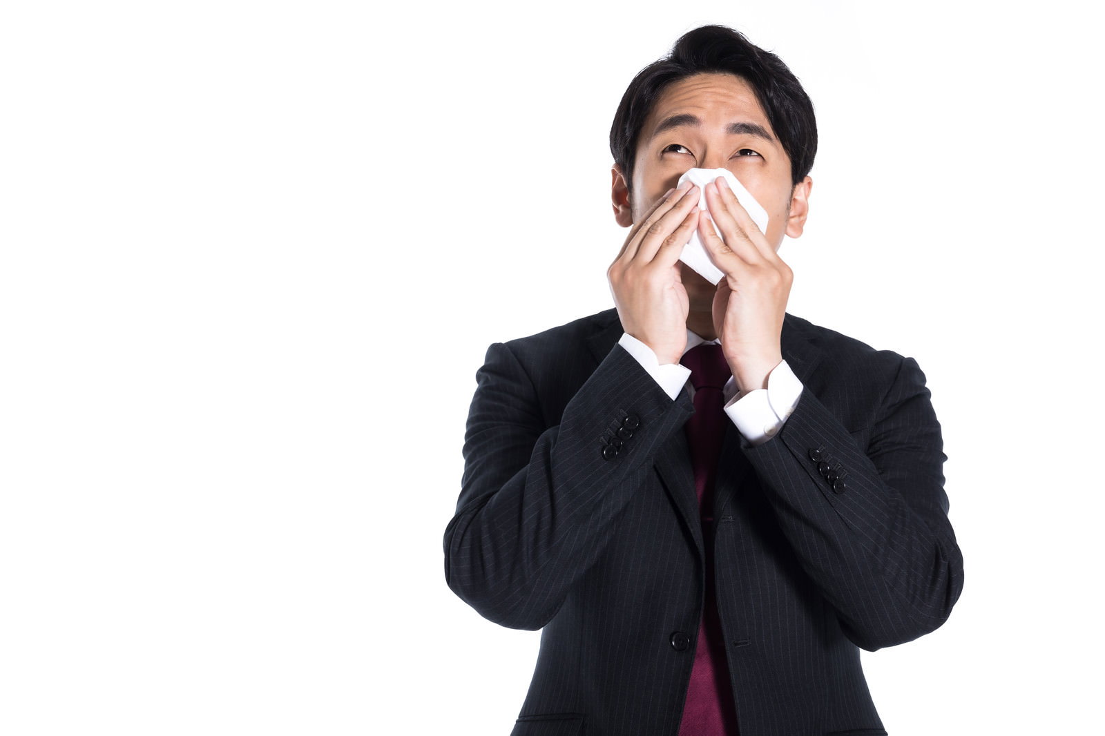 黒いスーツを着た男性がティッシュで鼻を押さえている［モデル：大川竜弥］