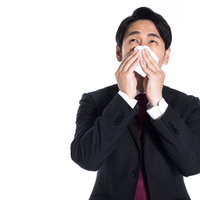 花粉症で鼻水が止まらず、ティッシュで鼻を押さえる会社員の写真