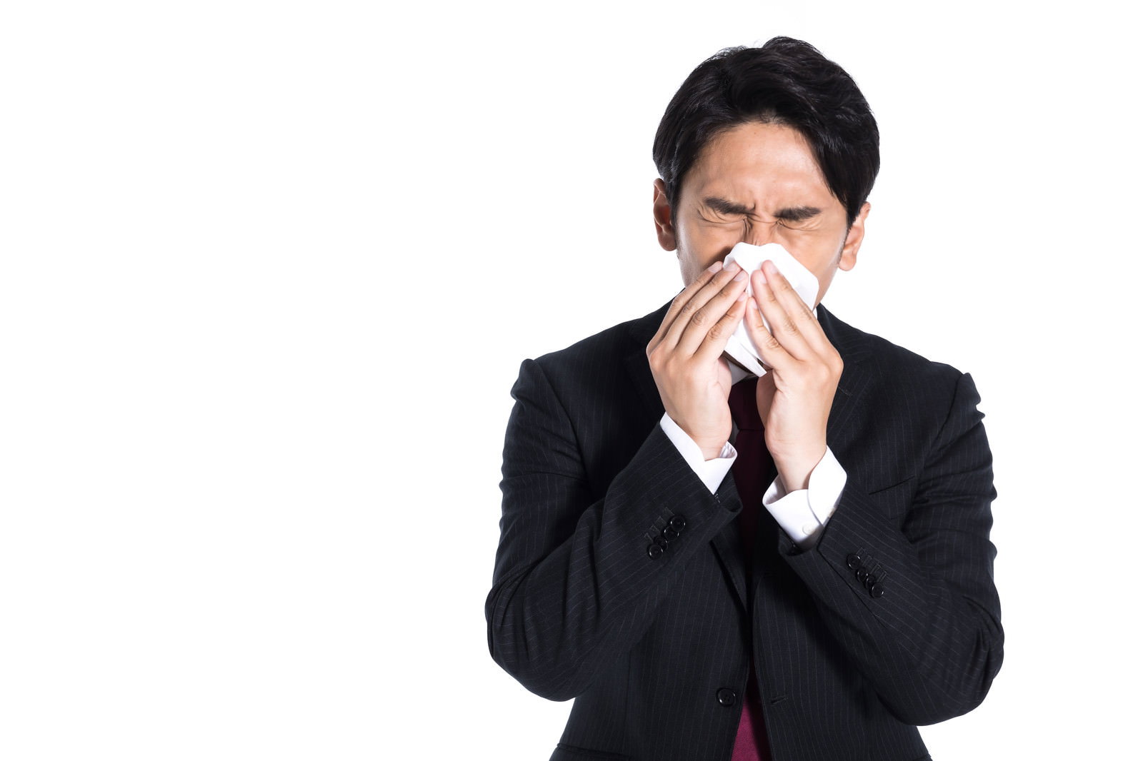白いティッシュで鼻をかんでいる黒いスーツ姿の男性［モデル：大川竜弥］