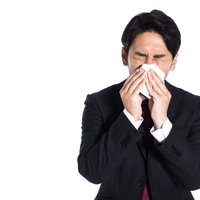 季節の変わり目に体調を崩してティッシュで鼻をかむ会社員の写真