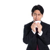 花粉症で目がショボショボする男性会社員がティッシュで鼻をかむの写真