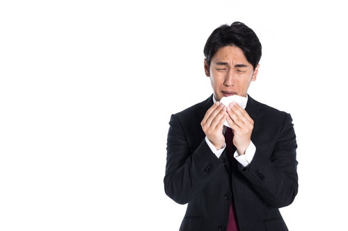花粉症で目がショボショボする男性会社員がティッシュで鼻をかむ