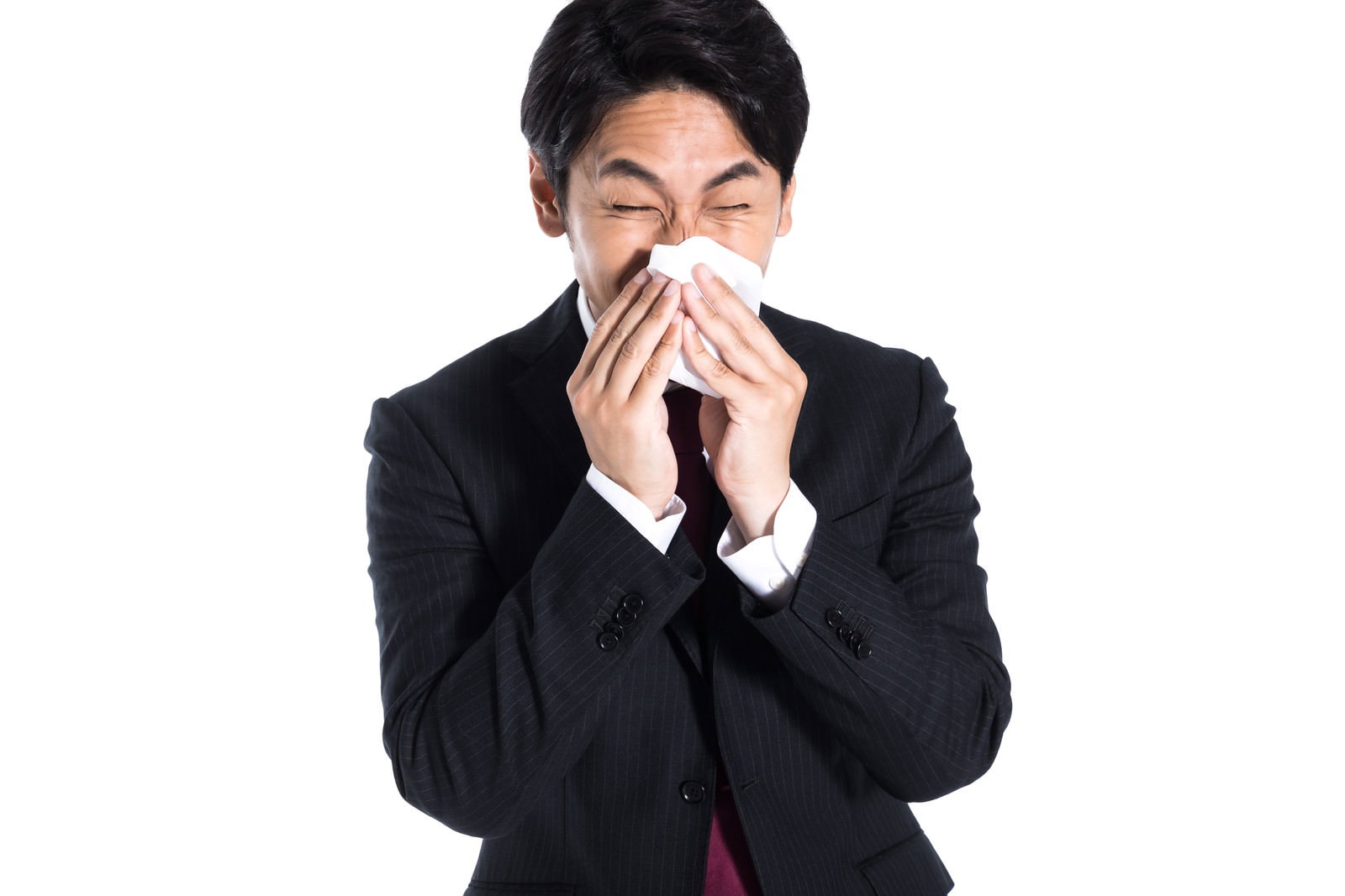 スーツ姿の会社員がティッシュで勢いよく鼻をかんでいる様子［モデル：大川竜弥］