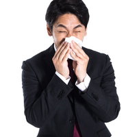 スーツ姿で勢いよく鼻をかむ会社員 ティッシュを手にした姿の写真