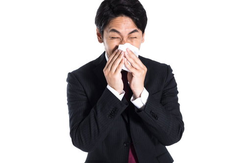 スーツ姿で勢いよく鼻をかむ会社員 ティッシュを手にした姿