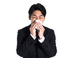 花粉症で鼻のムズムズが止まらない会社員がティッシュで鼻をかむの写真