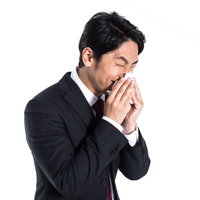 ティッシュで鼻をかむスーツ姿の男性、花粉症や風邪の症状の写真