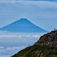 雲海の上に聳える富士山を望む岩場の登山者の写真