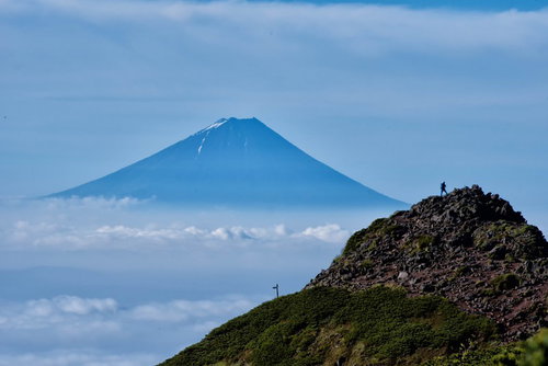 雲海の上に聳える富士山を望む岩場の登山者