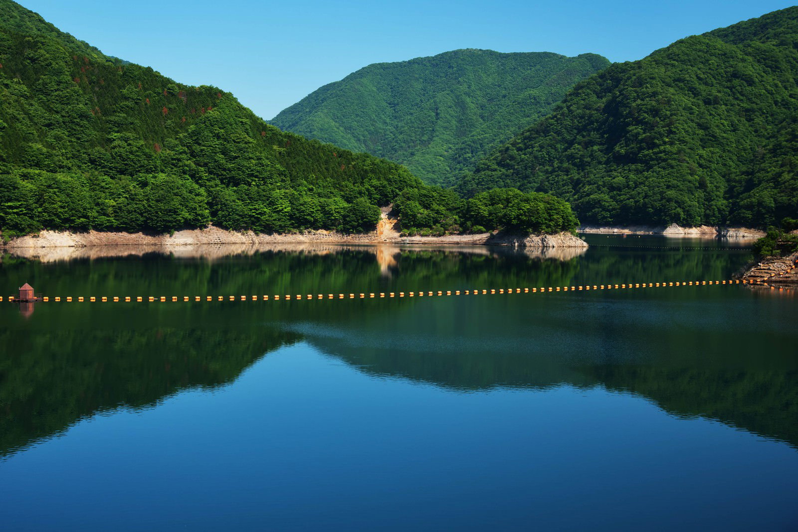 青空と山々が映り込む川治ダムの静かな湖面