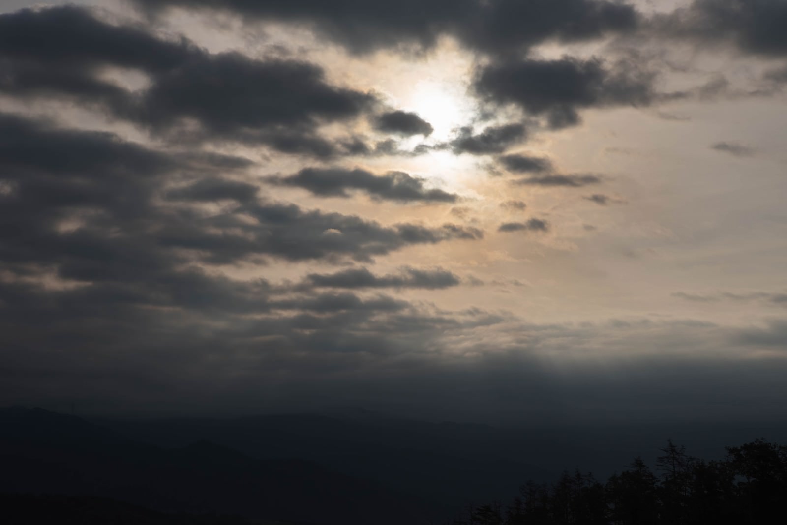 厚い雲が空を覆い雲間から薄明かりが差し込む夕暮れの空
