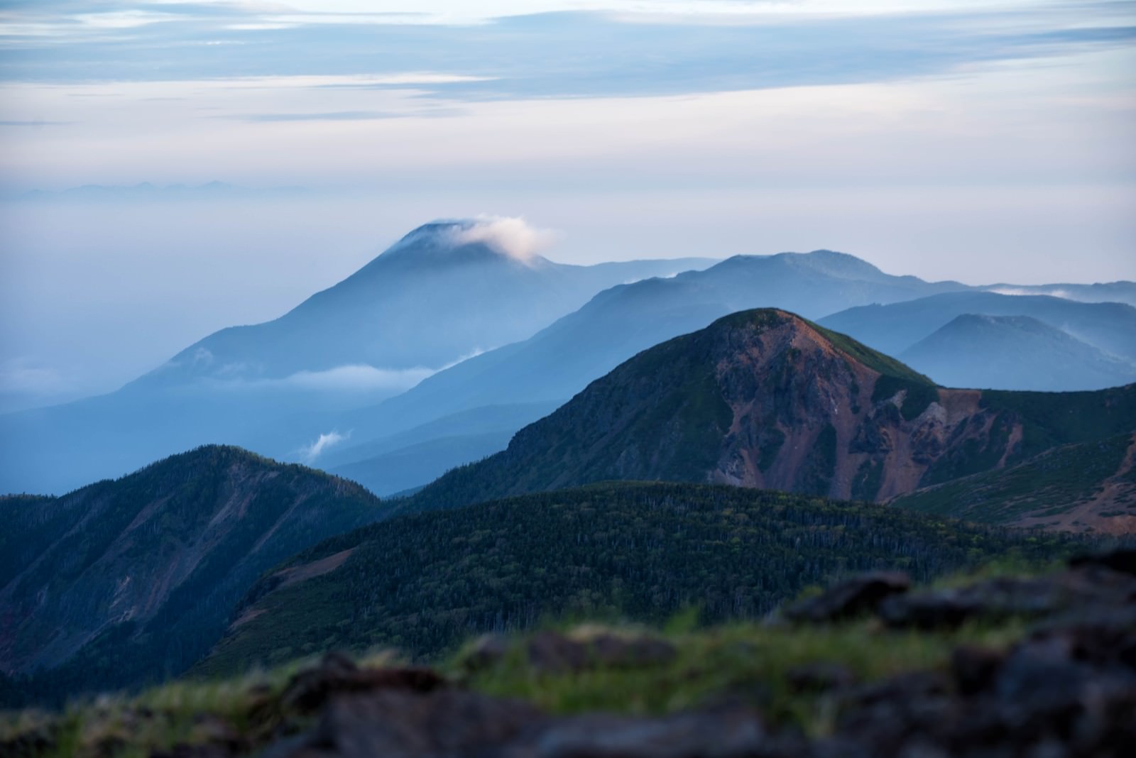 霞の中に浮かび上がる蓼科山と重なり合う山並みの風景