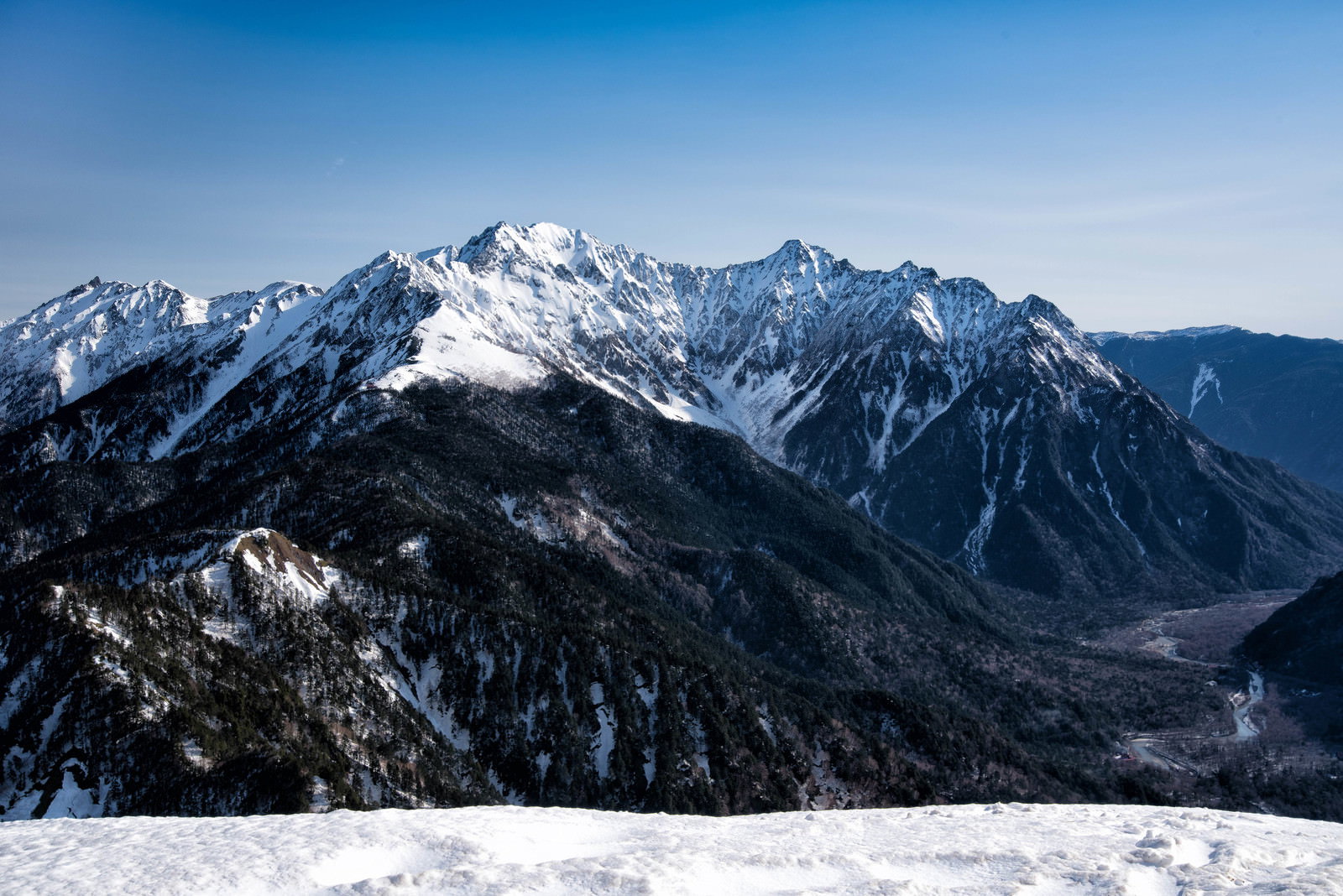 青空の下に雪化粧した穂高連峰の山々が連なる春の風景