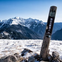 雪に覆われた焼岳山頂の道標と北アルプスの展望の写真