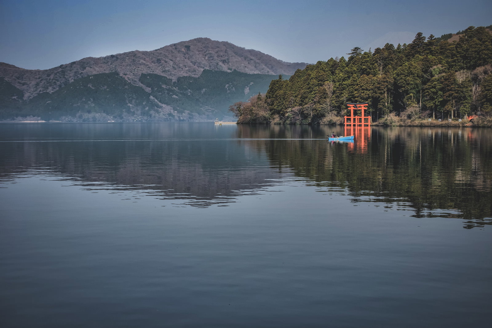 芦ノ湖に浮かぶ釣り船と箱根神社の朱色の鳥居、背景の山々