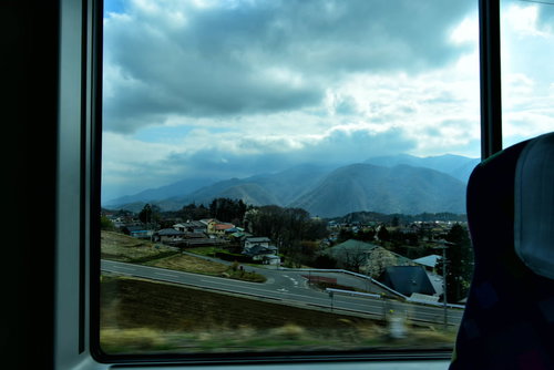 車窓から望む南アルプスの連なる山脈と住宅地の風景