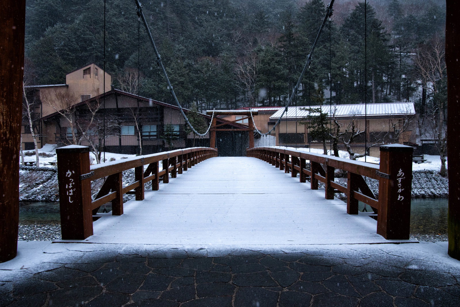 雪に覆われた河童橋と奥の山小屋群、背景に雪の山林が見える冬の上高地