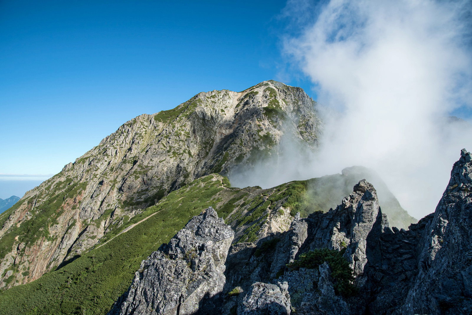 険しい岩稜の山々と青空に立ち上がる白い雲の山岳風景