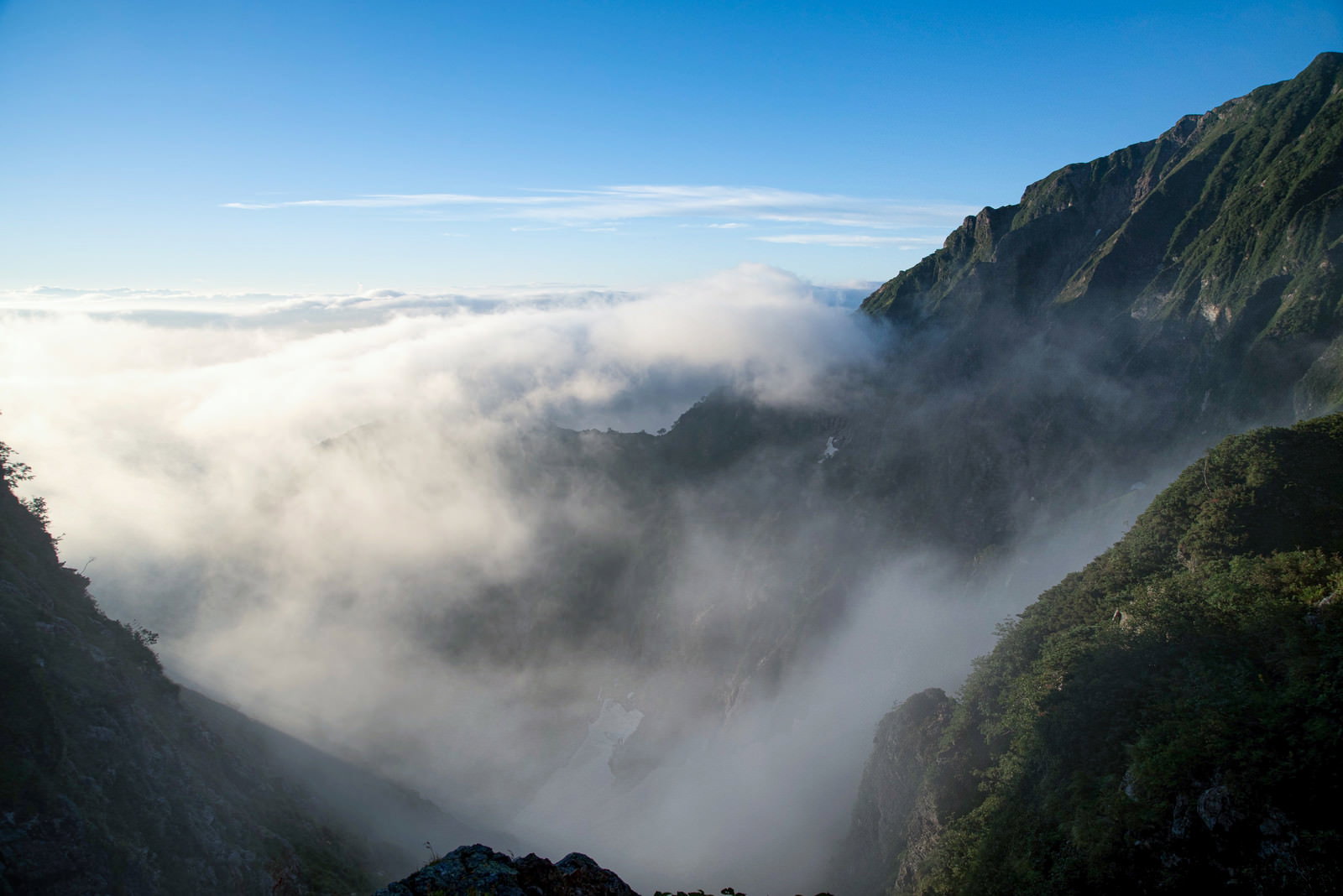緑の山肌と青空の間に白い雲海が流れ込む山岳風景