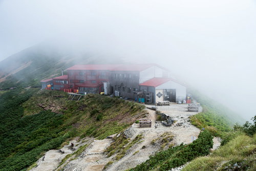 雲に覆われて佇む山荘と石畳の登山道を行く登山者