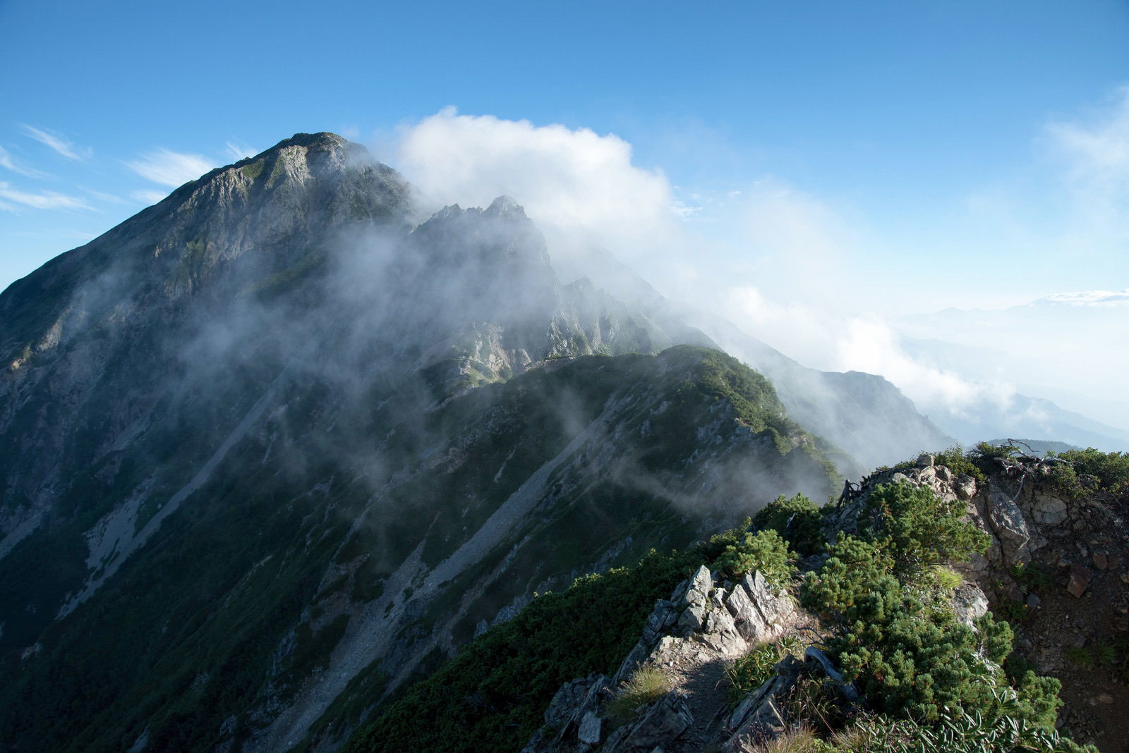 険しい岩稜に白い雲がかかる山岳風景