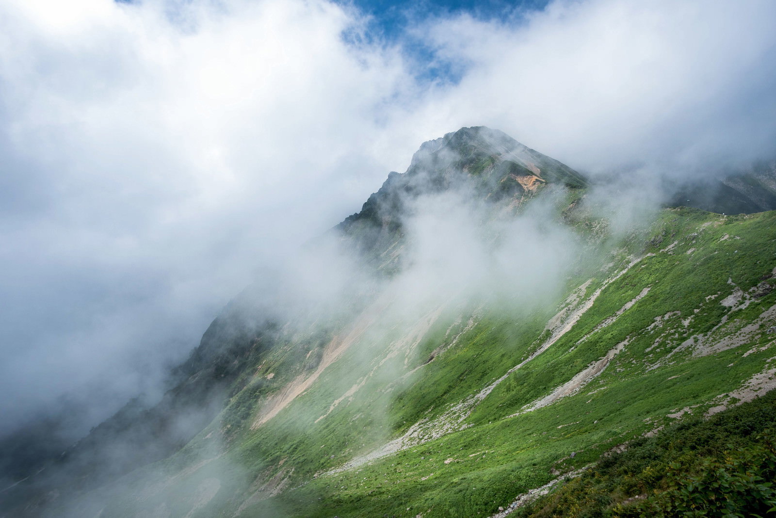 緑の山肌に白い雲が流れる山岳風景