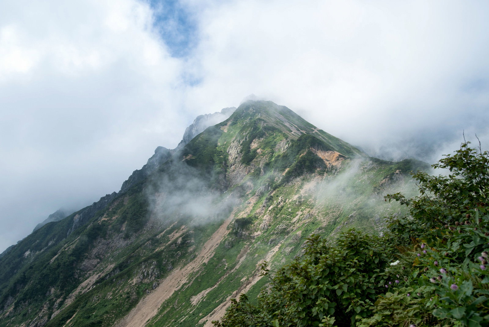 雲や霧に包まれた険しい山の尾根と岩肌が写された写真