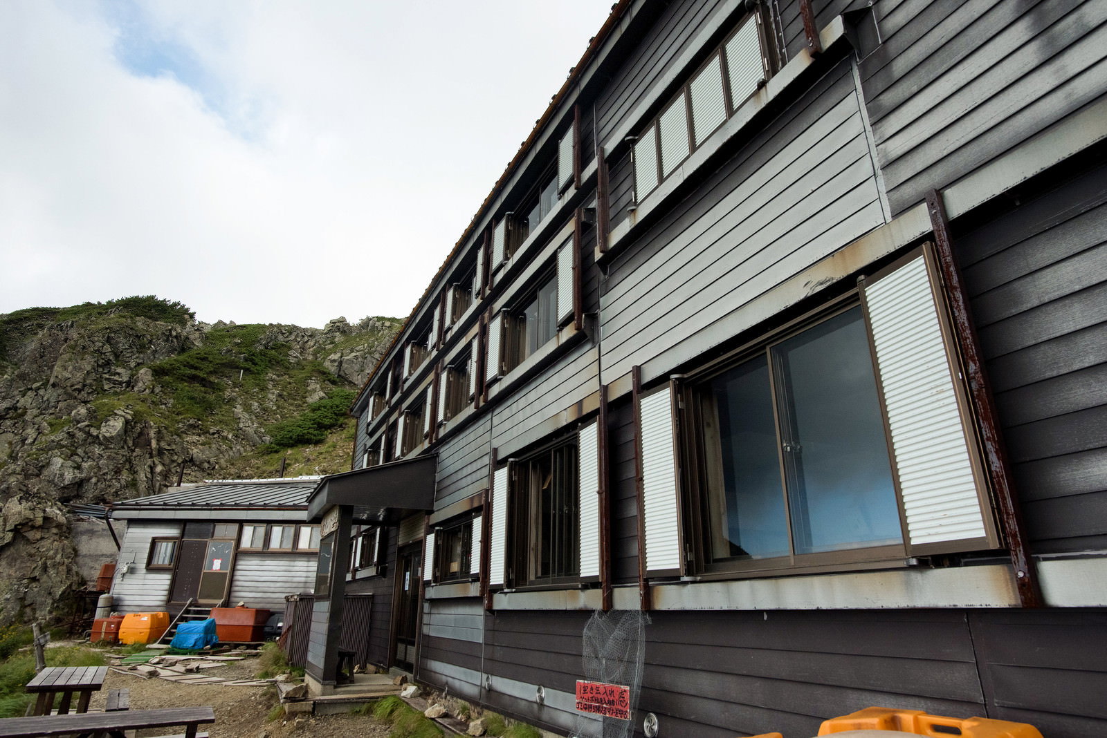 八峰キレットの緑の山間に建つグレーの外壁の山小屋