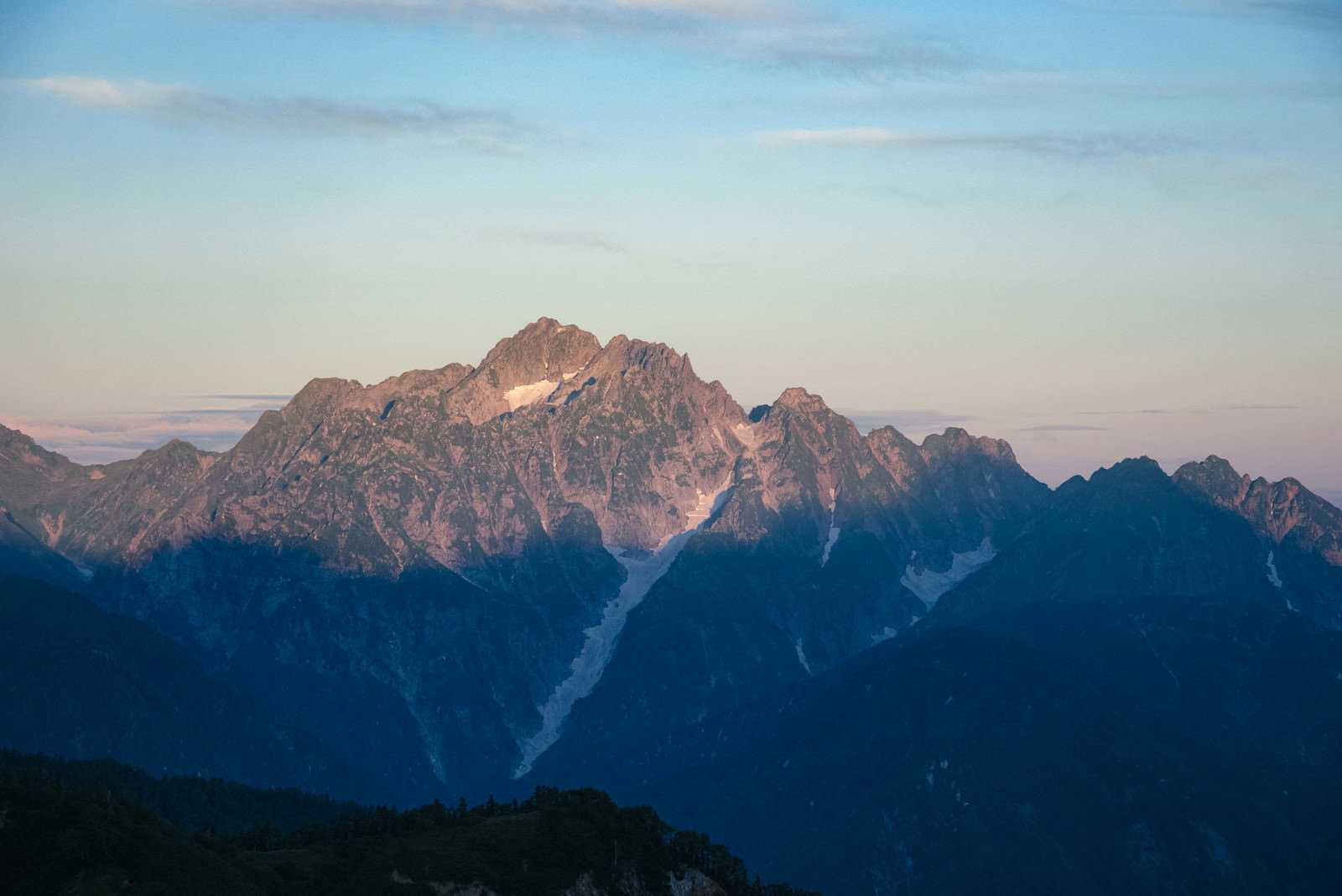 早朝の朝焼けに照らされた連峰のシルエットが重なる山岳風景
