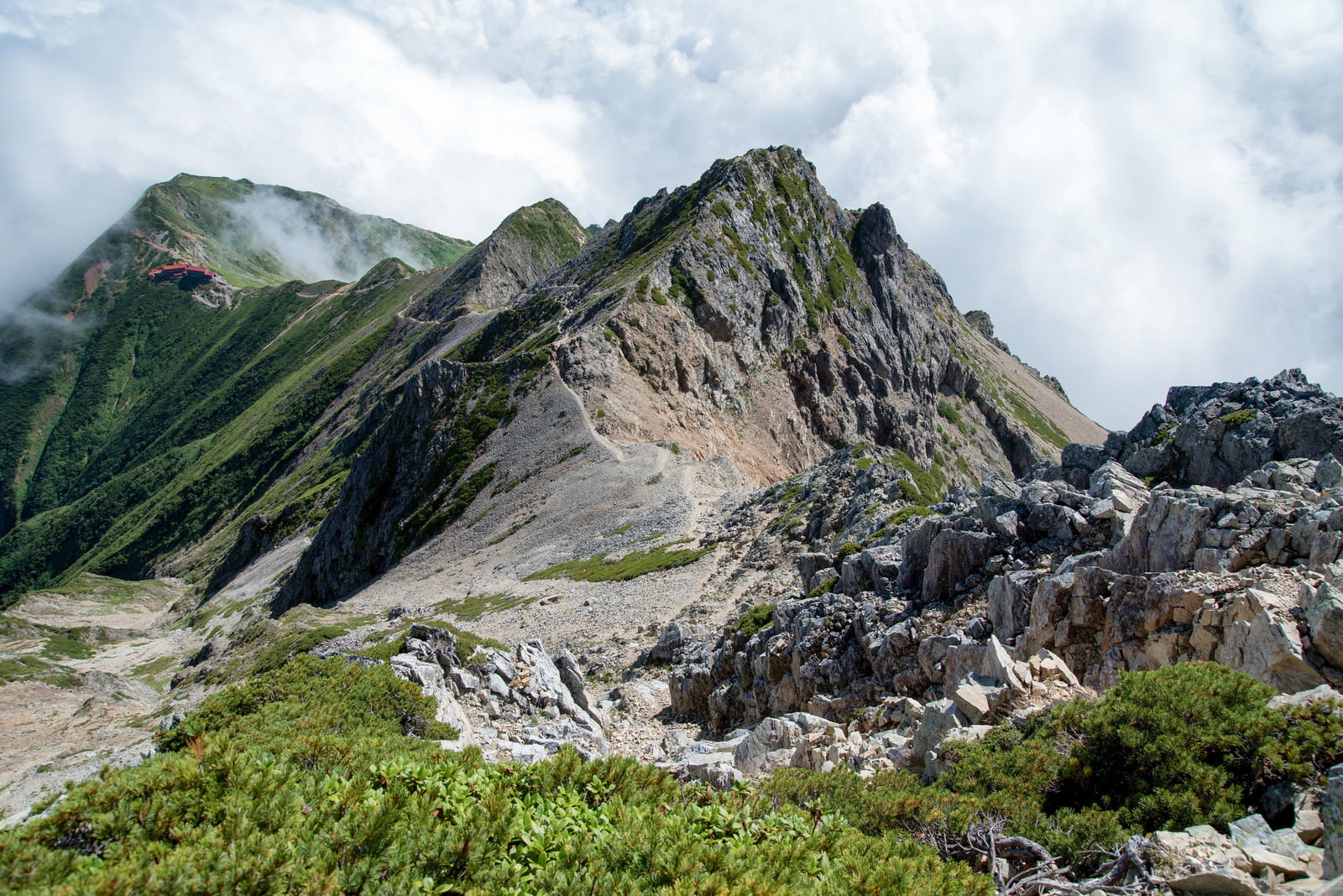 岩場の登山道を抜けた先に建つ山小屋と険しい山岳風景