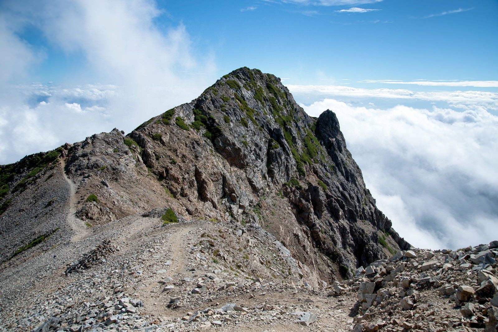 険しい岩稜が連なる稜線に続く登山道と眼下に広がる雲海