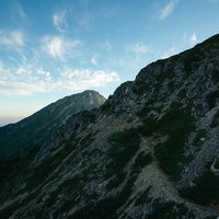 岩稜の傾斜面から続く登山道と青空、八峰キレットの岩尾根の写真